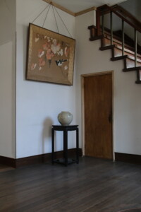 掛け軸風の絵画と陶器が静かに佇む、階段下の装飾スペース。昭和の迎えの美が感じられます。 旧高野寫眞舘の階段下にある壺と掛け軸画が飾られた装飾コーナー