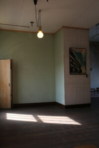 昭和の写真館らしい、ペンダント照明と緑色の壁が印象的なスタジオの一角。 旧高野寫眞舘の2階スタジオにあるレトロな照明とポスター、ひびの入った緑壁